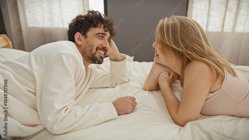 A smiling man and woman lying on a bed facing each other in a cozy bedroom, depicting a loving couple enjoying an intimate moment together. A smiling man and woman lying on a bed facing each other in a cozy bedroom, depicting a loving couple enjoying an intimate moment together.