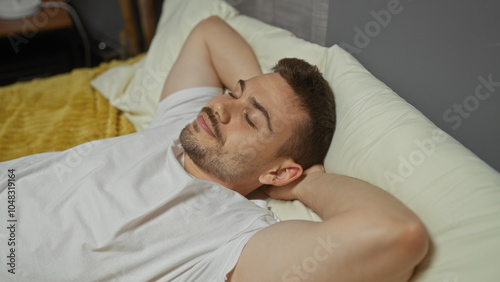 Handsome, young, hispanic, man with a beard relaxing in bed in a cozy bedroom, with his hands behind his head, enjoying a peaceful moment at home indoors.