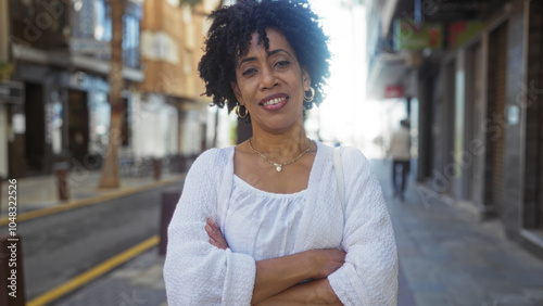 Beautiful african american woman with curly hair crossing her arms while standing confidently on a bustling urban street. photo