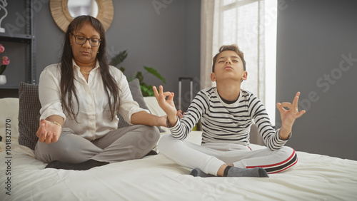 A woman and boy meditating together on a bed indoors, implying a calm family bonding moment