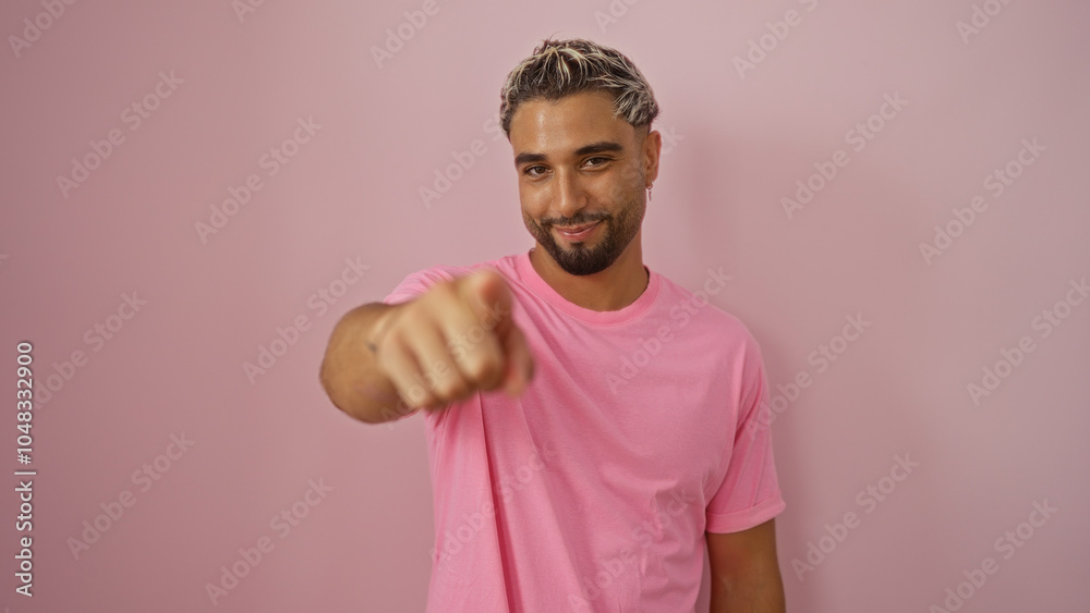 Handsome young arab man pointing towards the camera while standing against an isolated pink background Handsome young arab man pointing towards the camera while standing against an isolated pink background
