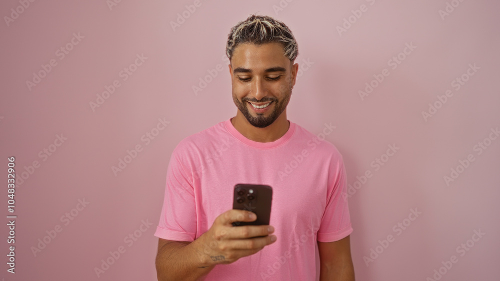 Fototapeta premium Young arab man with beard smiling at smartphone over isolated pink background