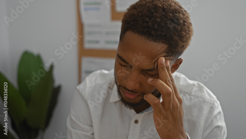 Young man stressed in an office room with indoor plants and documents on a bulletin board