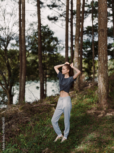 Young woman in casual sportswear stretching outdoors in a forest, surrounded by trees, showcasing a healthy and active lifestyle Nature and fitness concept