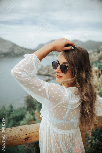 A beautiful girl in glasses bathing leaning on a wooden fence made of timber against the background of the sea and mountains