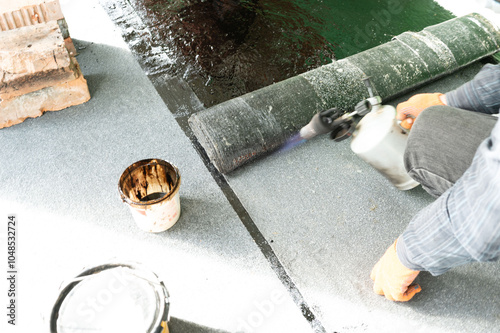 A man uses a kerosene lamp to heat a roll of bitumen for waterproofing the floor. photo