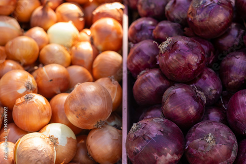 Fresh yellow and red onions displayed at an outdoor market during the afternoon sunlight