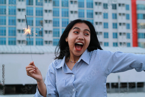 happy asian young business woman holding sparklers to celebrate new year eve standing in outdoor roof top with city building background