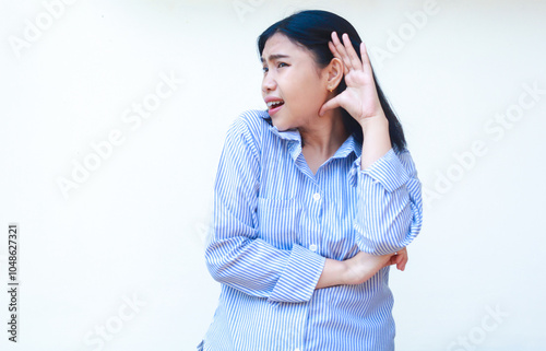 shocked asian woman eavesdropping with raising palms near ears wearing striped shirt isolated on white background photo