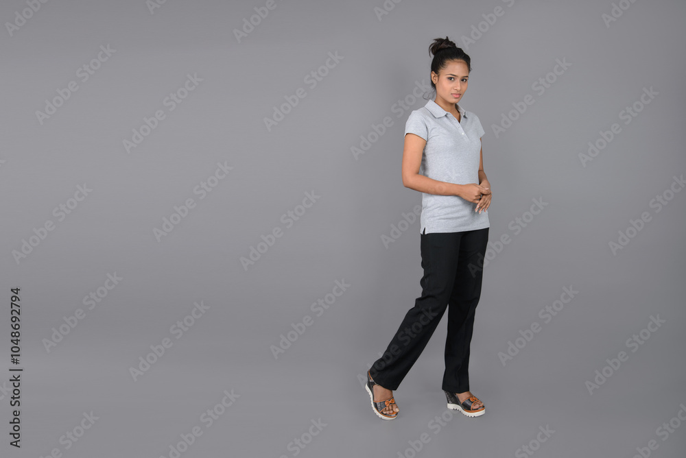 Young woman wearing grey polo t-shirt, black trousers and heels posing with cheerful expressions against grey background. Young woman wearing grey polo t-shirt, black trousers and heels posing with cheerful expressions against grey background.