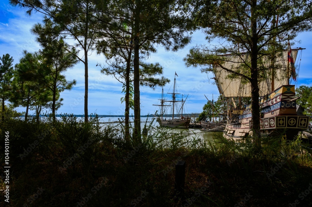 Tall ships docked at a serene harbor framed by trees. Tall ships docked at a serene harbor framed by trees.
