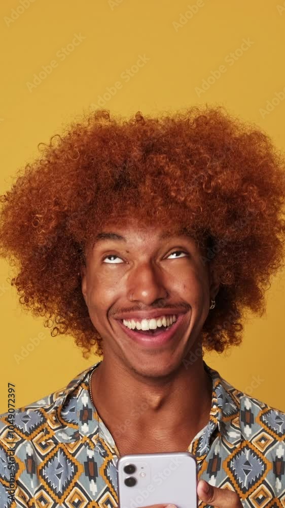 Happy guy using smartphone, looking up at advertising space isolated on yellow background in studio Happy guy using smartphone, looking up at advertising space isolated on yellow background in studio
