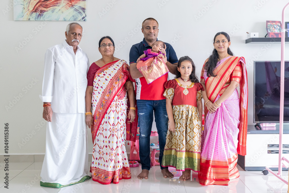 Obraz premium An Indian family wearing traditional and casual costumes spends time with their baby, girl and grandparents in a high-rise apartment building in Kuala Lumpur, Malaysia. June 2024