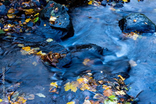 Fallen autumn leaves and rocks in a stream with long exposure