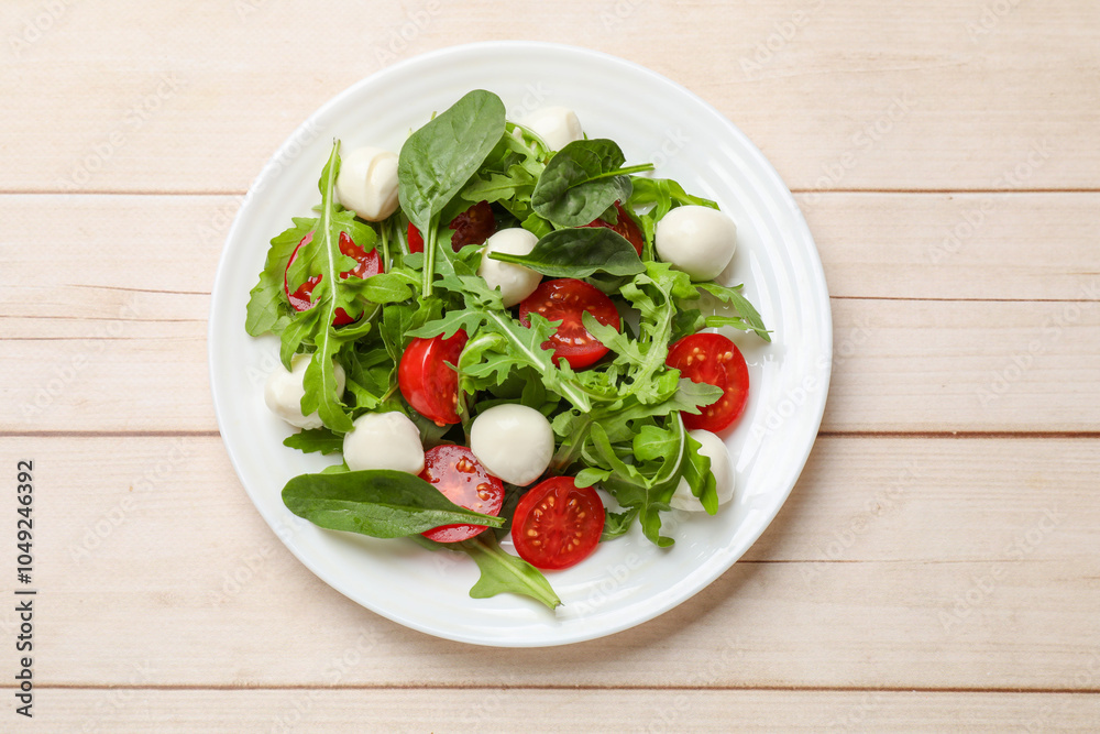 Tasty salad with arugula, spinach, mozzarella cheese and tomatoes on wooden table, top view Tasty salad with arugula, spinach, mozzarella cheese and tomatoes on wooden table, top view