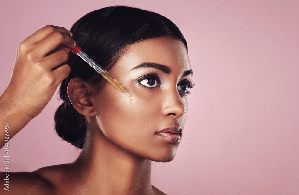 Obraz premium Face, skincare serum and serious woman in studio isolated on a pink background mockup. Dermatology, cosmetics and Indian model with hyaluronic acid, essential oil or vitamin c dropper for skin health