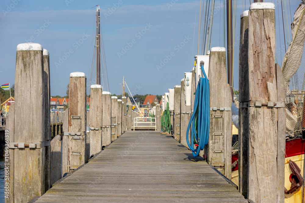 Obraz premium Wooden bridge pier in harbor on Terschelling island, Sidewalk way by haven or quay shore, The Dutch Wadden sea, A municipality and an island in the northern, Friesland, West-Terschelling, Netherlands