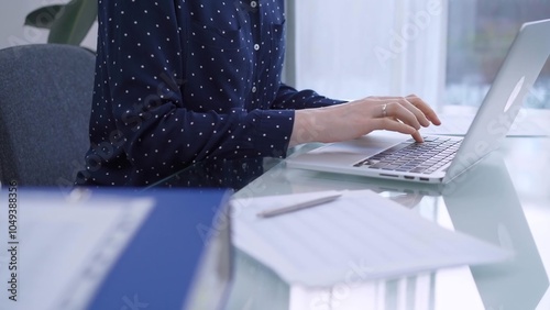 A female accountant or businesswoman with blue dotted blousy is typing on laptop computer on glass desk in the office. Business people concept photo