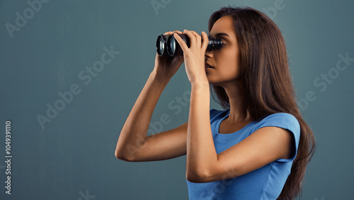 Young woman searching with binoculars on blue background