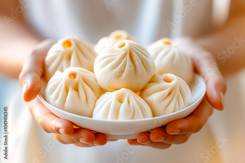 A beautiful assortment of fluffy bao buns rests on a white plate, cradled in hands, showcasing their intricate detailing against a warm, inviting ambiance