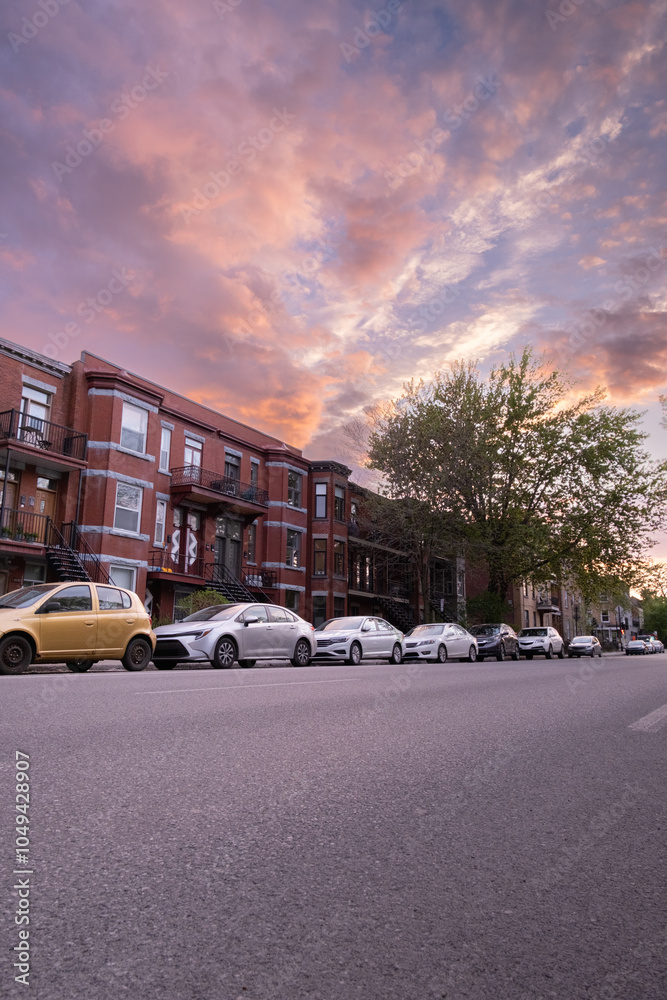 Fototapeta premium Cars parked in front of houses in a street, stunning sunset. Montreal, Canada - 27th March 2024