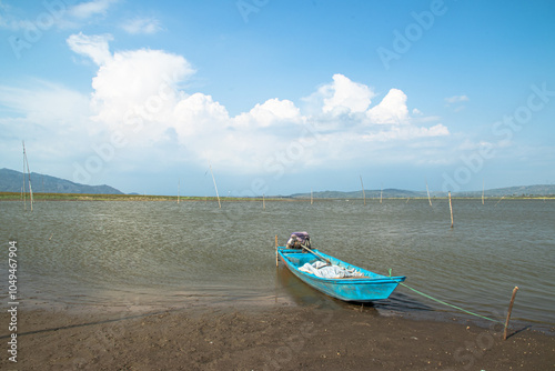 a serene view of a lake with blue sky in the background. There is a simple blue boat resting on the water's edge. photo