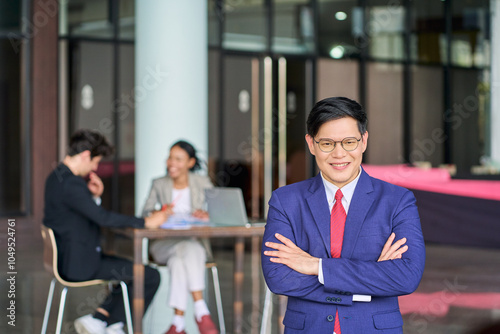 Smile face of asian businessman in navy blue suit is portraiting with team in background for confirm quality of work concept. photo