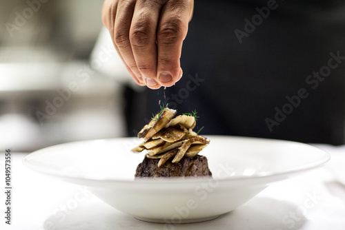 Person sprinkling salt over mushrooms and brown meat in white plate