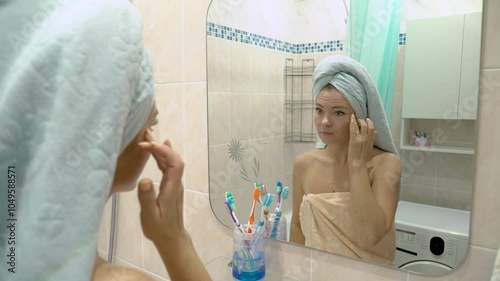 Pretty young woman in a towel looks in the bathroom mirror