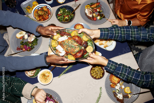 Top view of unrecognizable man passing homemade baked chicken to friend at dining table served with variety of festive dishes during Christmas dinner, camera flash, copy space photo