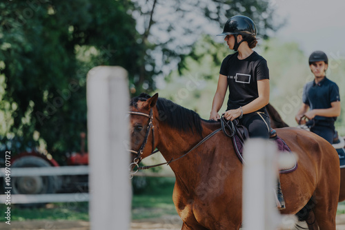 Two young equestrians ride horses outdoors, enjoying a sunny day. The image captures the focus and skill required in horseback riding amidst a lush green setting.