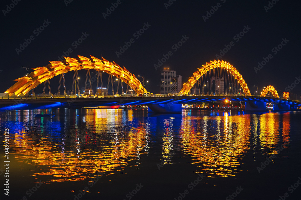 Fototapeta premium Dragon Bridge over the Han River is a famous landmark in the city of Da Nang in Vietnam at night with a golden backlight