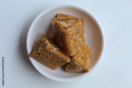 Enting-enting in triangle shape. Enting-enting is crushed peanuts mixed with sugar, Indonesia traditional snack. On small white bowl, isolated on white background photo