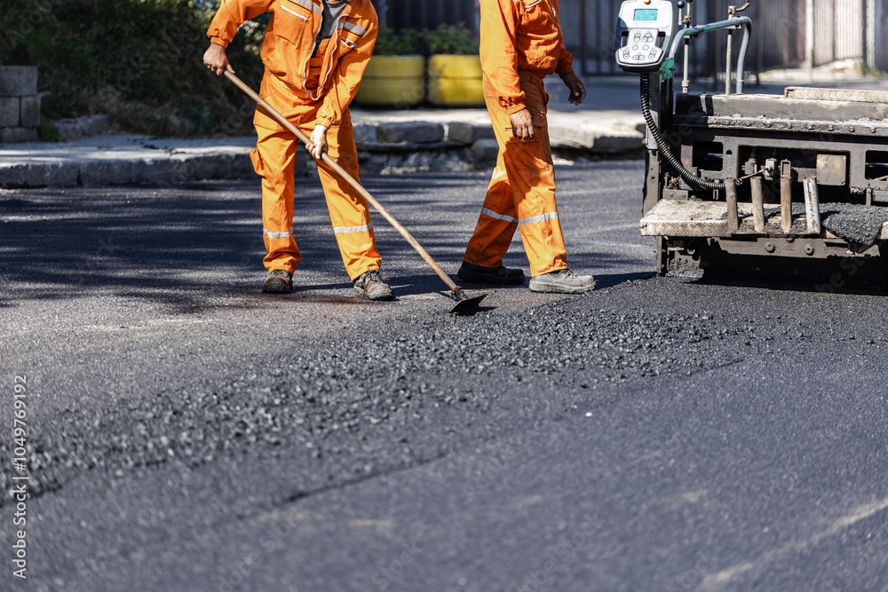 Foto de Two construction workers in orange uniforms laying asphalt on a ...