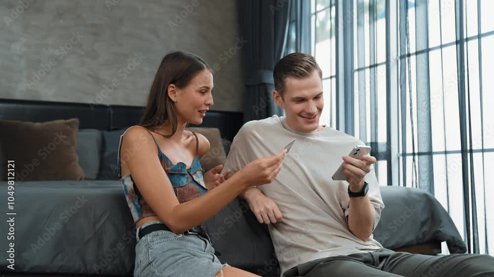 Young couple sit in the home bedroom using online payment app and digital wallet on smartphone to pay with credit card. E commerce shopping and modern purchasing via mobile internet. Adit Young couple sit in the home bedroom using online payment app and digital wallet on smartphone to pay with credit card. E commerce shopping and modern purchasing via mobile internet. Adit