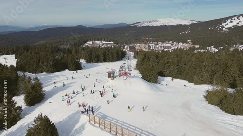 Alpine ski lift aerial drone view in Kopaonik, Serbia. Chairlift at ski resort, mountain winter forest top down rising shot. Pine trees covered with snow. Active lifestyle