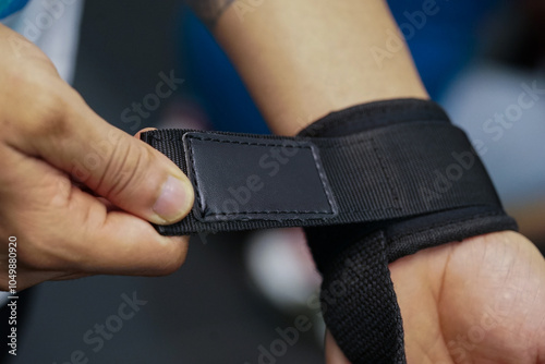 Close-up of a person's hands gripping a barbell, wearing a wrist support or strap. sneakers are visible, suggesting a workout session at a gym.