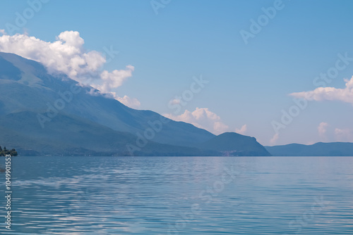 Serene lakeside scene along the shoreline of  Lake Ohrid, North Macedonia. Mountain range of National Park Galicica in the distance. Slopes and hills covered with lush green vegetation and forest photo