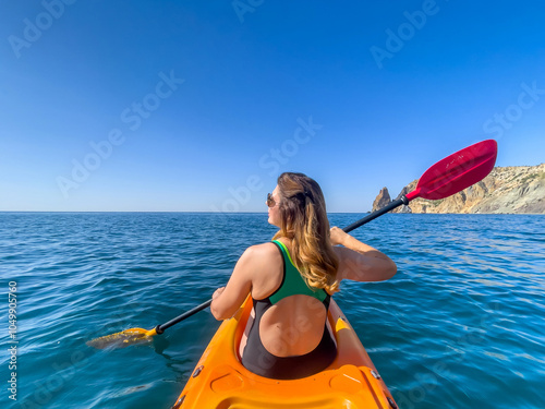 Kayaking Woman Sea Adventure - A woman in a kayak paddles on a calm sea while enjoying a scenic view. photo