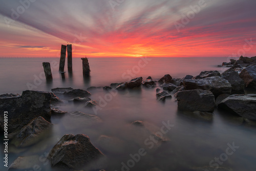 Stones and poles in the IJsselmeer under a morning red cloudy sky. A spectacular red sky above the IJsselmeer near Den Oever (Netherlands). A magic sere morning. photo