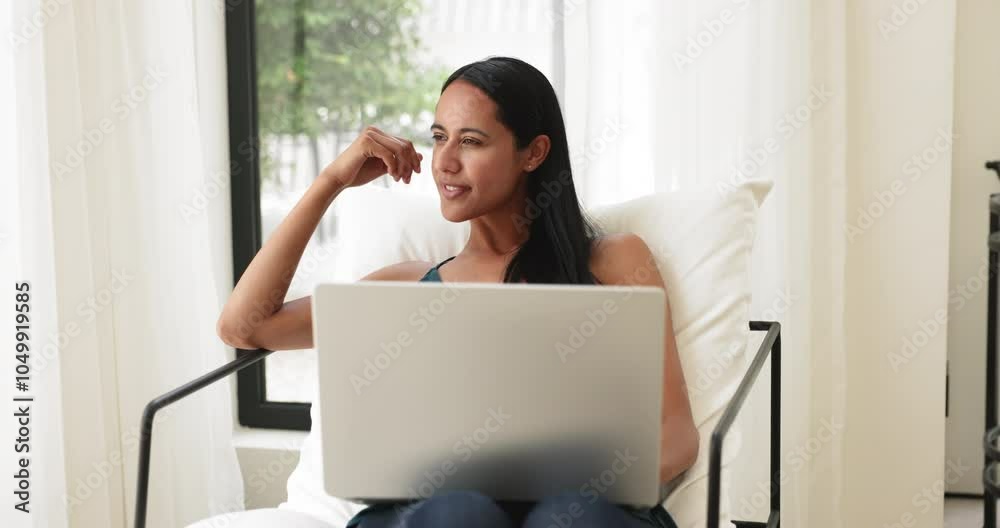 Attractive woman sitting on comfortable armchair with modern laptop indoors, studying, learning new platform or program, ponder on blog post, e-mailing, chatting online, working on-line using internet
