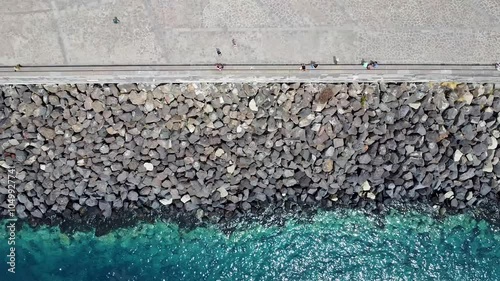Top-down aerial view of a stone breakwater along a coastal walkway