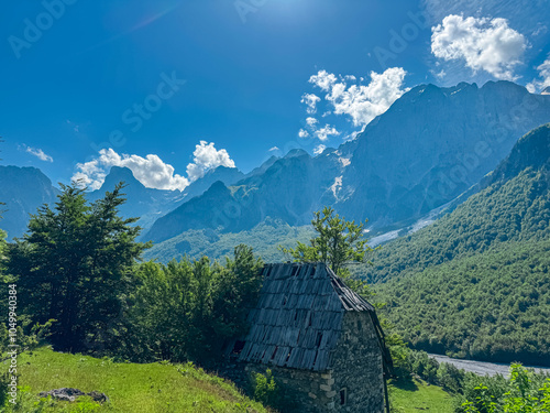 Rustic abandoned wooden cabin nestled in alpine forest surrounded by majestic mountain peaks of massif Zhaborret, Albanian Alps, Valbone Valley National Park, Albania. Weathered decaying roof photo