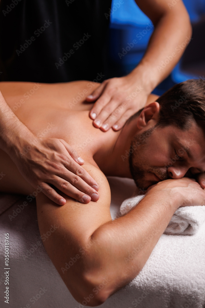 Handsome man having restorative shoulder massage in spa, enjoying relaxing atmosphere, rebooting after work. Masseuse performs therapeutic massage of the injured hand of visitor, restoring health. Handsome man having restorative shoulder massage in spa, enjoying relaxing atmosphere, rebooting after work. Masseuse performs therapeutic massage of the injured hand of visitor, restoring health.