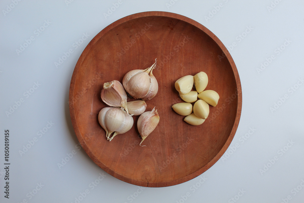 Garlic cloves or bulb, before and after peeled, on wooden plate, isolated on white background, flat lay or top view Garlic cloves or bulb, before and after peeled, on wooden plate, isolated on white background, flat lay or top view