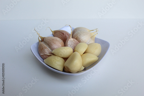 Garlic cloves or bulb, before and after peeled, on white bowl, isolated on white background photo