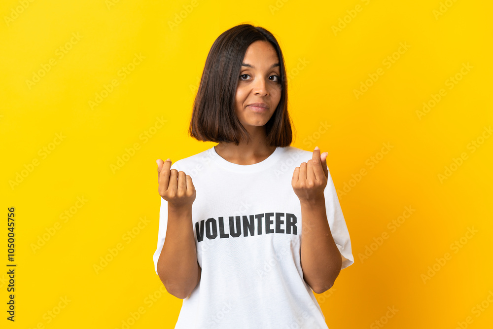 Young volunteer woman isolated on yellow background making money gesture Young volunteer woman isolated on yellow background making money gesture