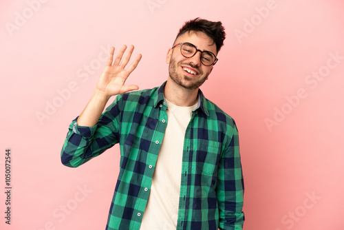 Young caucasian man isolated on pink background saluting with hand with happy expression