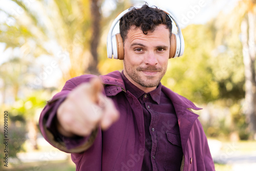 Young caucasian man at outdoors listening music and pointing to the front