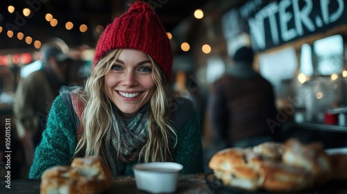 A cheerful woman in a red knit hat smiles warmly in a cozy setting with pastries in the foreground, exuding a sense of warmth and happiness on a winter day.